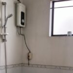 Nhà tắm gia đình với bình nóng lạnh gắn tường phía trên khu vực vòi sen, nền gạch ướt